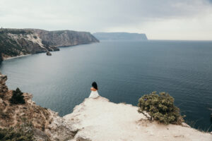 A woman sits at a cliffside overlooking the sea